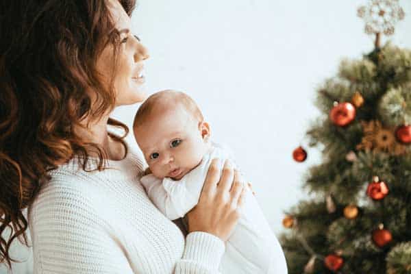 mom holding baby in front of christmas tree